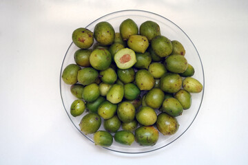 Green and ripe umbu fruits (Spondias tuberosa) on a plate. They are also known as Brazil plums. A fruit cut open in cross-section.  The fruits are edible, sweet and sour and also good for diabetes.