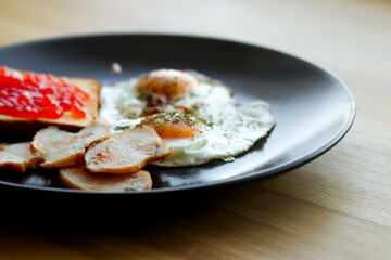  a delicious American-style breakfast plate featuring a fried egg, crispy bacon, and a touch of red caviar. American breakfast on the black plate close up