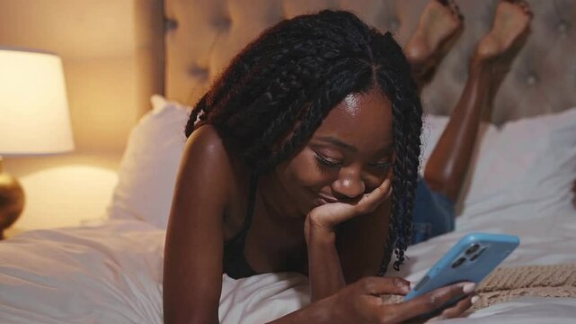Woman lying pronated on her bed using her smartphone at night.
