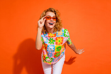 Stylish young woman with red hair wearing sunglasses and a colorful floral print t-shirt against an orange background