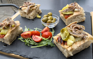 restaurant appetizer of focaccia topped with anchovies with tomatoes leeks and olives on the side (slate plate presentation) in koper slovenia mediterranean cuisine diet food seafood meal healthy