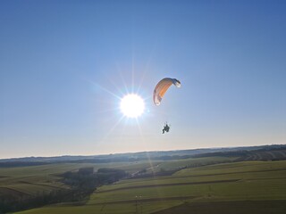 Aerial view of powered paraglider flying over mountainous landscape and forests, concept of adventure sports and aerial freedom