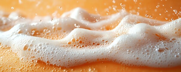 Fototapeta premium Flowing white foam and bubbles on orange liquid surface creates dynamic texture with splashing droplets and frothy waves in macro photography.
