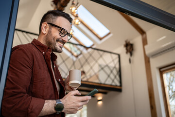 Smiling freelancer enjoying morning coffee and checking smartphone at home
