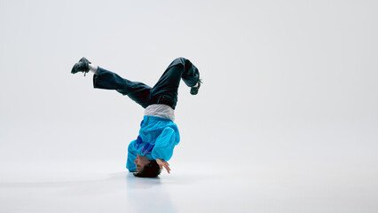 Dynamic street dancer, dressed vintage attire, spinning on head with legs extended in air against...
