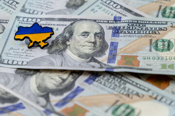 Hundred dollar bills are scattered on the table. Pin The pin in the form of the map of Ukraine lies...