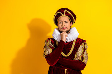 Thoughtful young man in renaissance nobleman costume against yellow backdrop highlighting historic...