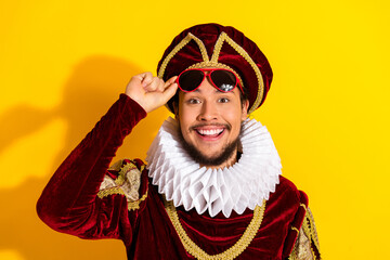 Young man dressed as a nobleman in a historic costume with sunglasses against a vibrant yellow...