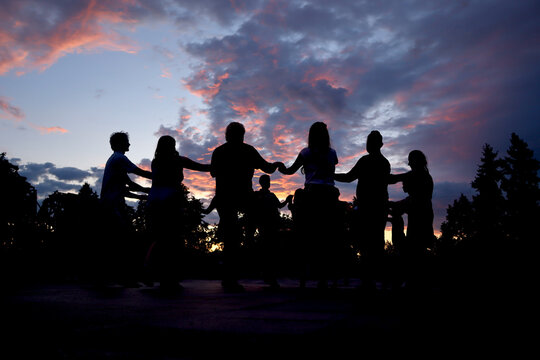 Silhouettes of people dancing a circle folk dance in the street at sunset.