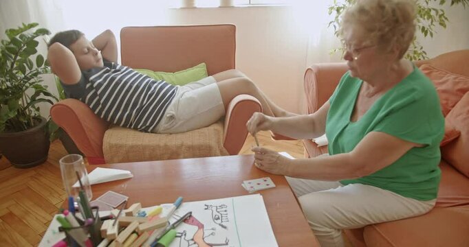 A grandmother and her grandson enjoy quality time together, playing cards in their cozy living room. This heartwarming scene captures the joy of family and inter generational connection.