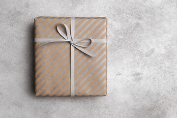 Gift box with bow and striped craft paper decoration on grey stony table, top view