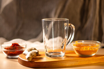 Empty transparent cup on wooden tray with turmeric and chili species. Mock up for design. Served table. Preparation for making drink