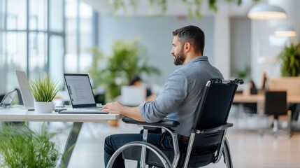 Inclusive Workspace: A determined professional, seated in a wheelchair, navigates his laptop in a modern office environment.