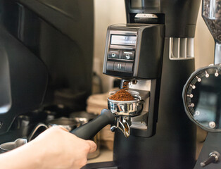 Barista grinding fresh organic coffee beans in a portafilter with a professional electric grinder.