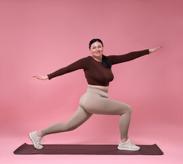 Plus size woman in gym clothes exercising on pink background