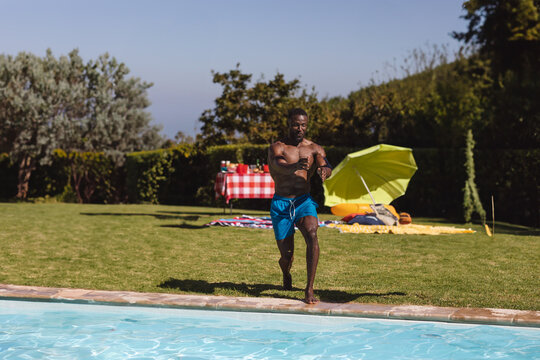 Man running towards pool, enjoying summer day at outdoor party with friends, copy space