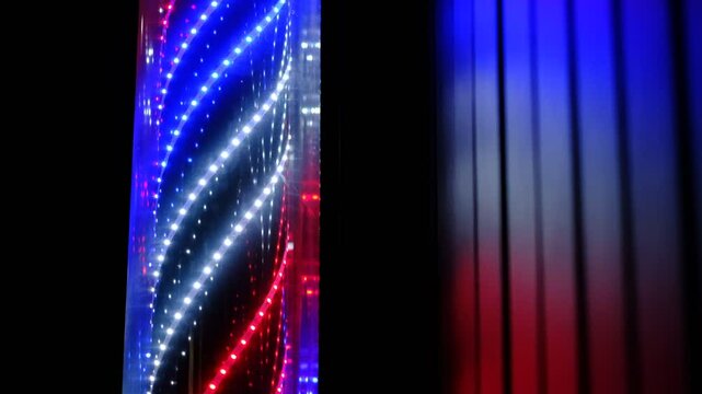 A neon lighted barber pole with red, blue and white lights. The pole is lit up and is in a dark room