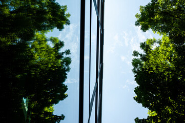  Futuristic city building with glass walls reflecting trees and sky, emphasizing harmony between...