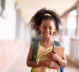 Smiling girl holding book in school hallway, ready for class