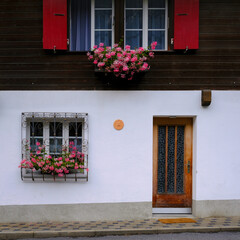 Swiss house front and decorative wood door, exterior with white walls, red shutters, and pink...