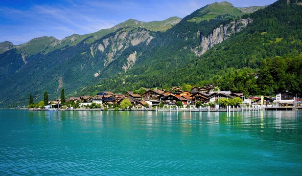 View of homes from boat on Lake Brienz in Switzerland with turquoise aqua blue water surrounded by scenic mountains. 