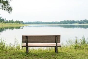 Obraz premium serene landscape with empty wooden bench facing calm lake symbolizing tranquility and introspection