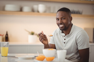 Smiling man enjoying breakfast cereal at home with orange juice on table, copy space