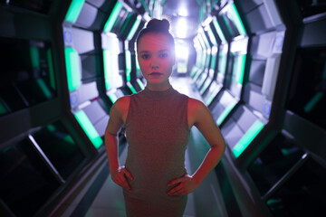 In futuristic corridor, confident woman standing with hands on hips, looking determined