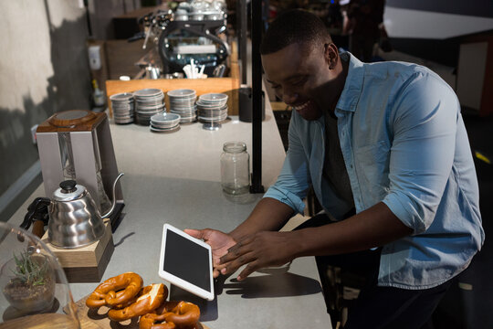 Smiling man using tablet at cafe counter with fresh pretzels nearby, copy space - Powered by Adobe