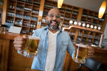 Smiling man holding beer mugs in lively bar with wooden shelves