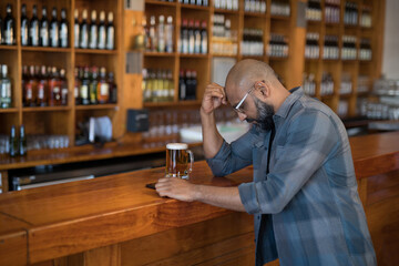 Man at bar with beer, looking thoughtful, surrounded by bottles on shelves, copy space