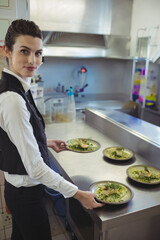 Server in restaurant kitchen preparing plates of gourmet food with smile, copy space