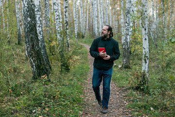 Fototapeta premium a bearded man walking through the forest with a red book and looking into the forest