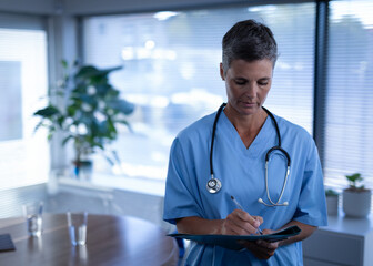 Healthcare professional in blue scrubs writing on clipboard in modern medical office, copy space