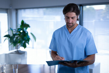 Medical professional in blue scrubs writing on clipboard in modern office