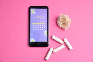 Smartphone with period calendar application, tampons and flower on pink background, flat lay