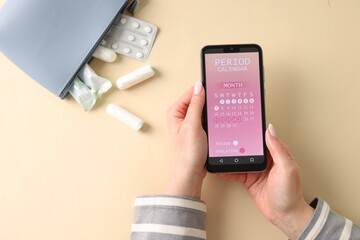 Menstruation. Woman holding smartphone with period calendar application on beige background, top view