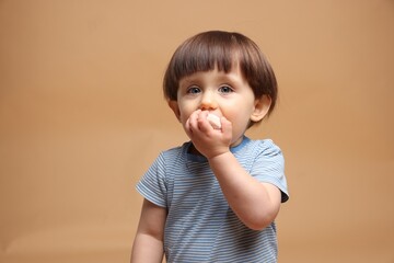 Cute little child eating tasty mochi on light brown background