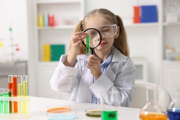 Little girl doing chemical experiment at desk indoors