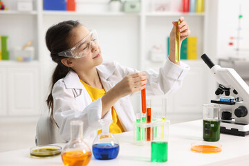 Little girl doing chemical experiment at desk indoors