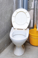 There is a toilet that has its lid raised positioned beside a yellow bucket