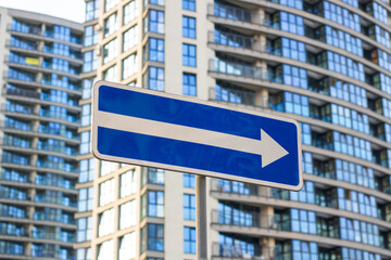 A blue and white street sign with a right arrow by a tall building