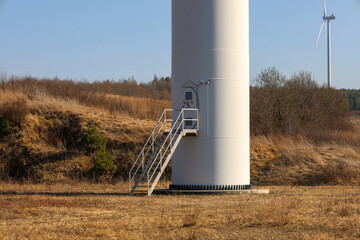 This photograph captures a close-up of the base of a wind turbine standing in a field. The wind...