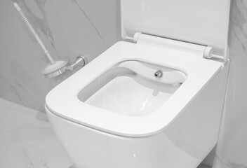 Wall hung automatic toilet. White ceramic toilet bowl on a marble wall. On the floor tiles.
