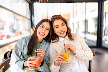 Two smiling friends drinking healthy juice at a cafe