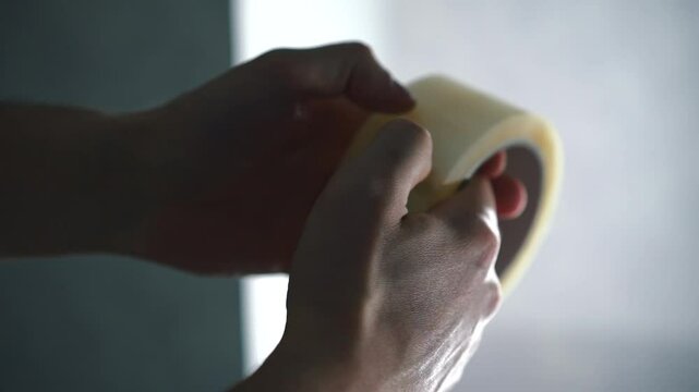 A roll of scotch tape in a man's hands, close-up.
Look for the edge of the tape.
Unpack the roll of scotch tape, scrape with a fingernail
