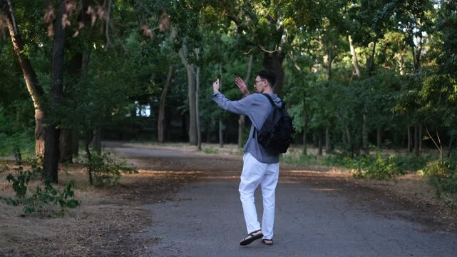 Young man blogger walks in the park on a sunny summer morning recording vlogs