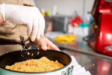 Pastry chef sprinkling crumbs into cake mold, preparing dessert in professional kitchen