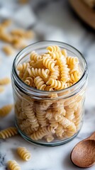  Glass jar filled with uncooked fusilli pasta on marble countertop. Soft lighting enhances rustic, homey kitchen atmosphere with Italian culinary charm.