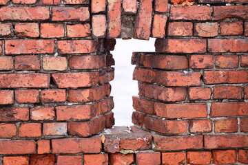A white cross sticking out of a worn-out brick wall.